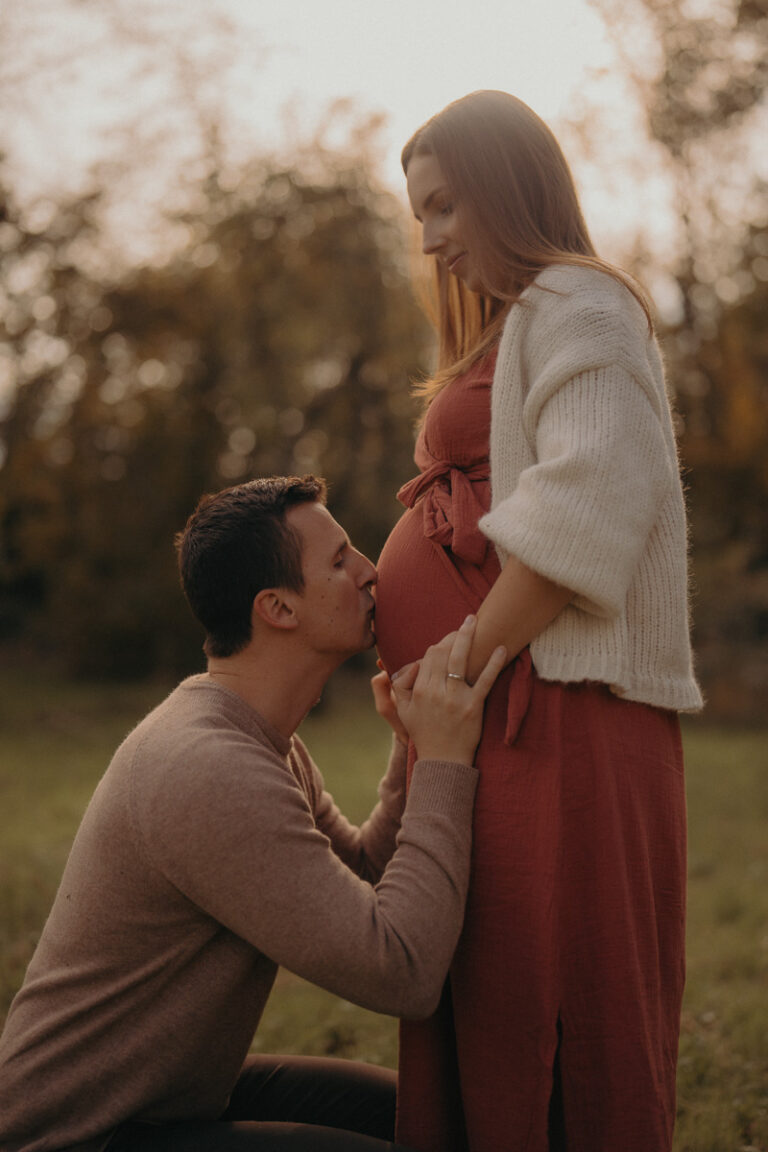 Partner küsst liebevoll den Babybauch während eines herbstlichen Outdoor-Babybauchshootings in Langen