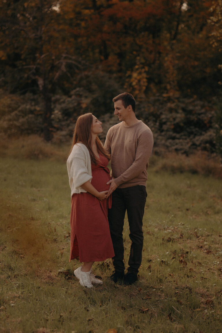 Werdende Eltern stehen eng umschlungen beim Babybauchshooting in der Natur im Herbst