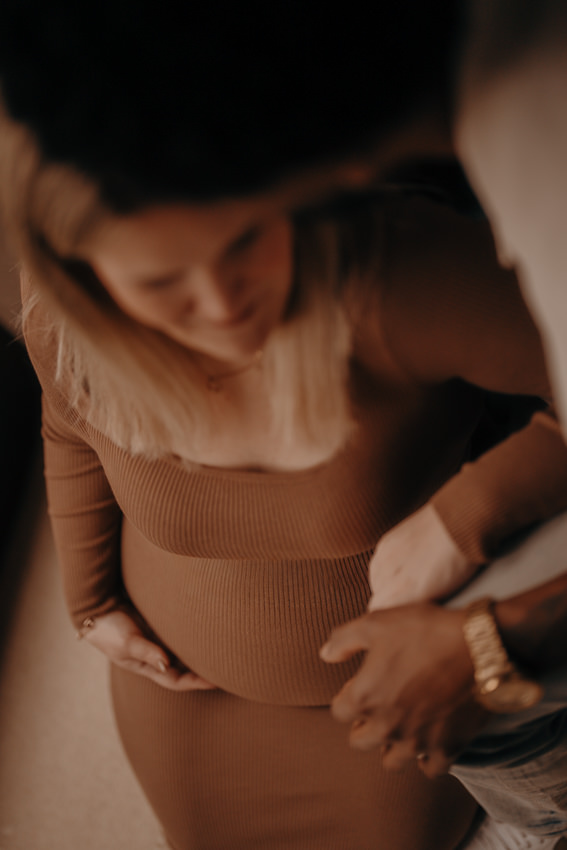 Babybauch Homestory: Schwangere Frau in den Armen ihres Partners, inniger Moment zuhause