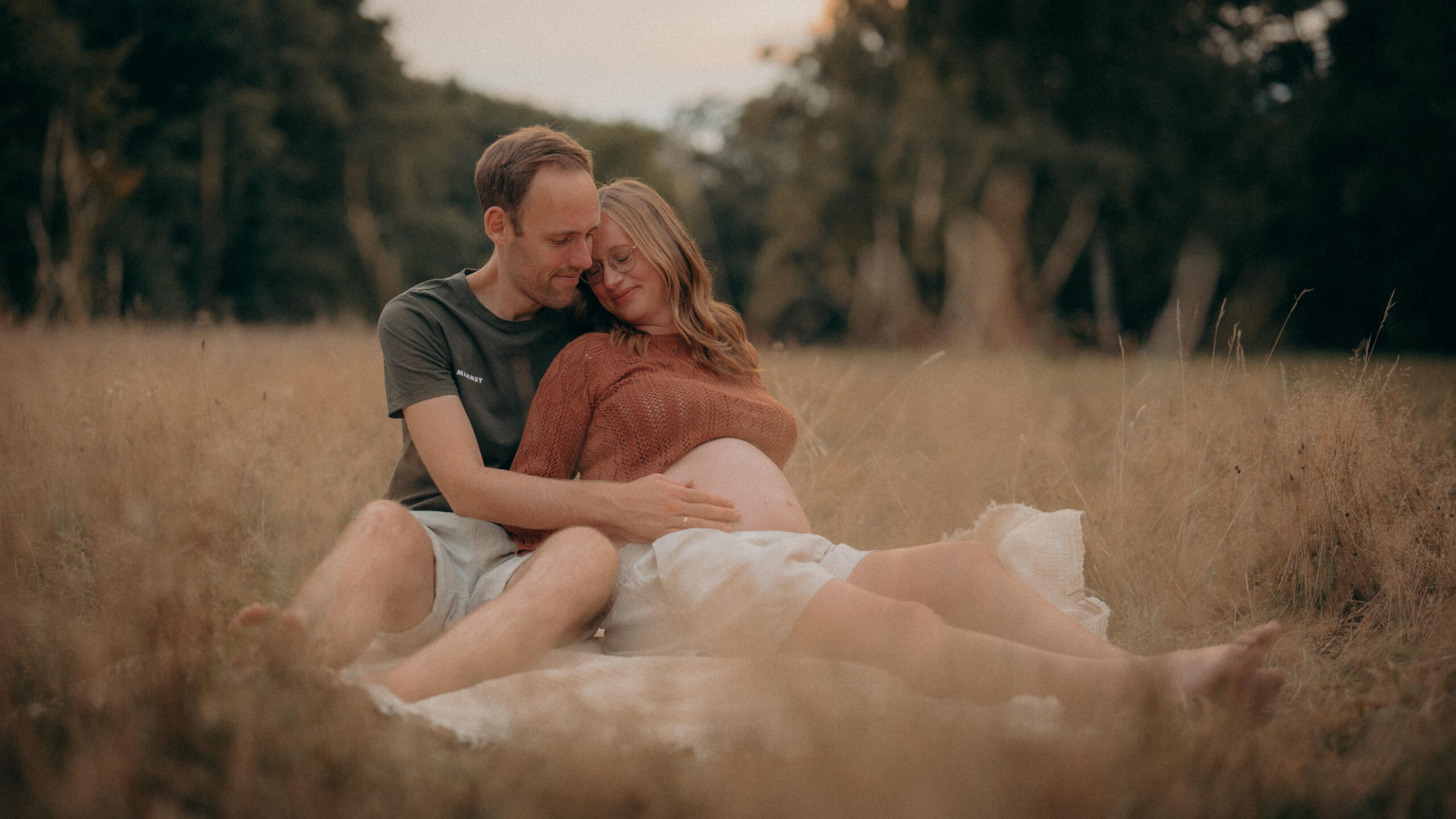 Babybauchshooting Frankfurt – schwangeres Paar in der Abendsonne auf einer Wiese.